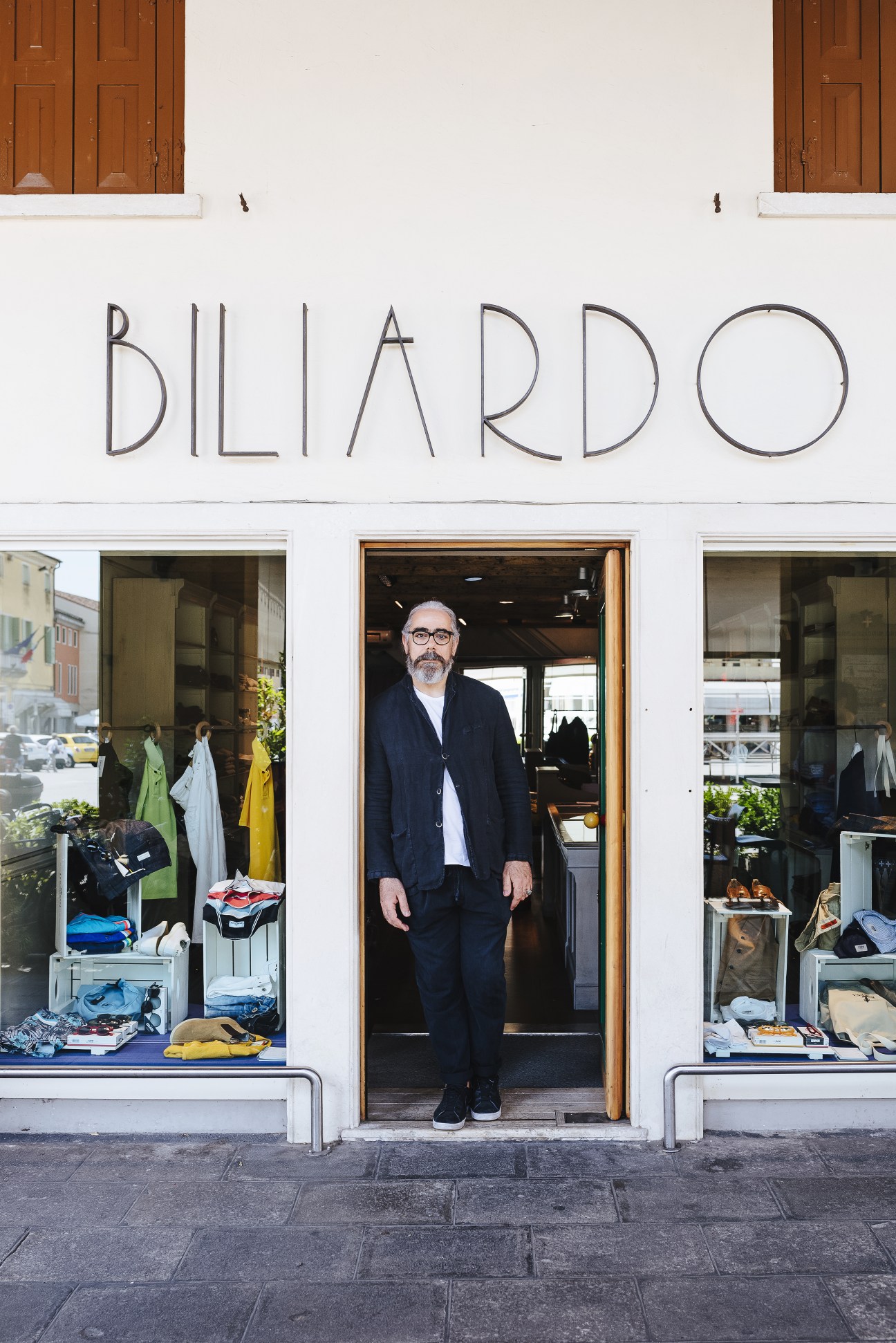 Man standing in doorway of Biliardo menswear shop with clothing visible in windows