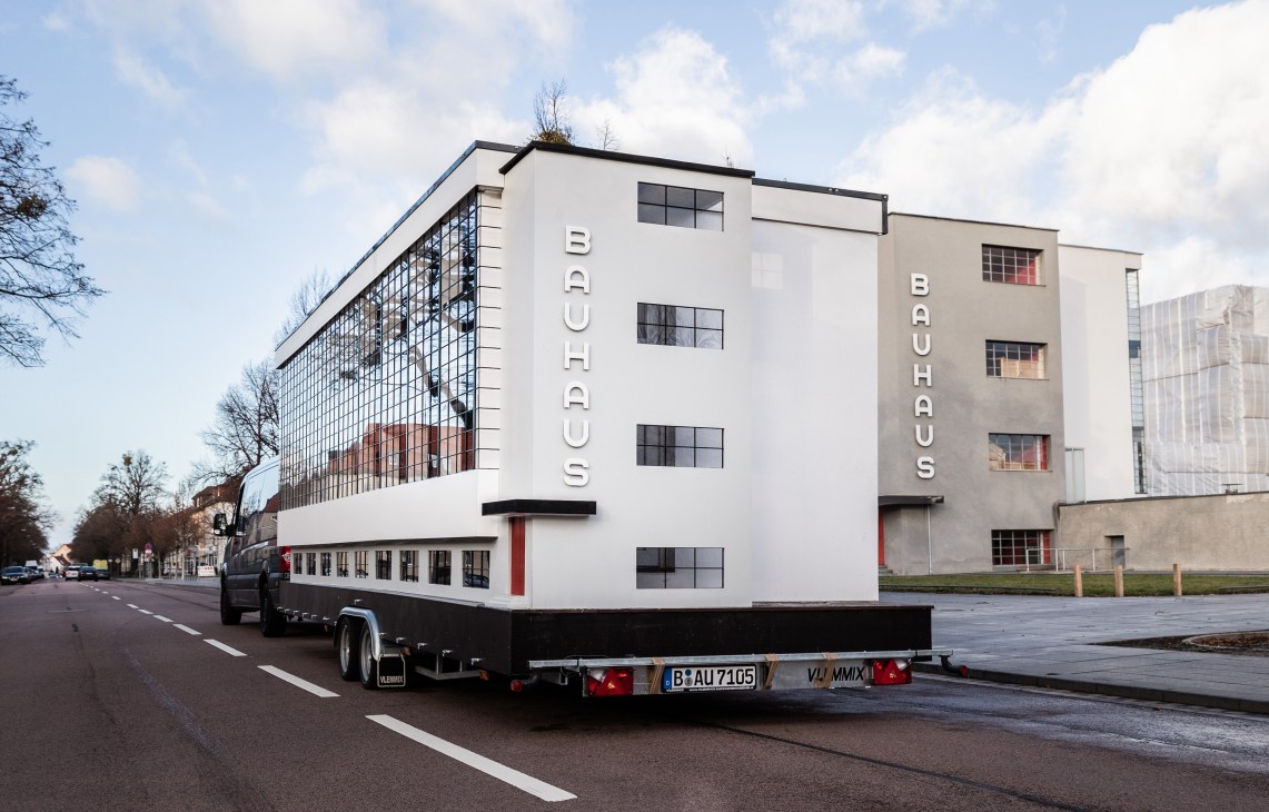 A mobile tiny home designed as a replica of the Bauhaus workshop building, towed on a street.