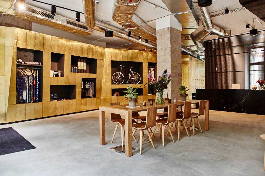 Interior of Becycle fitness studio in Berlin with wooden display shelving, dining table, and exposed brass ducting.