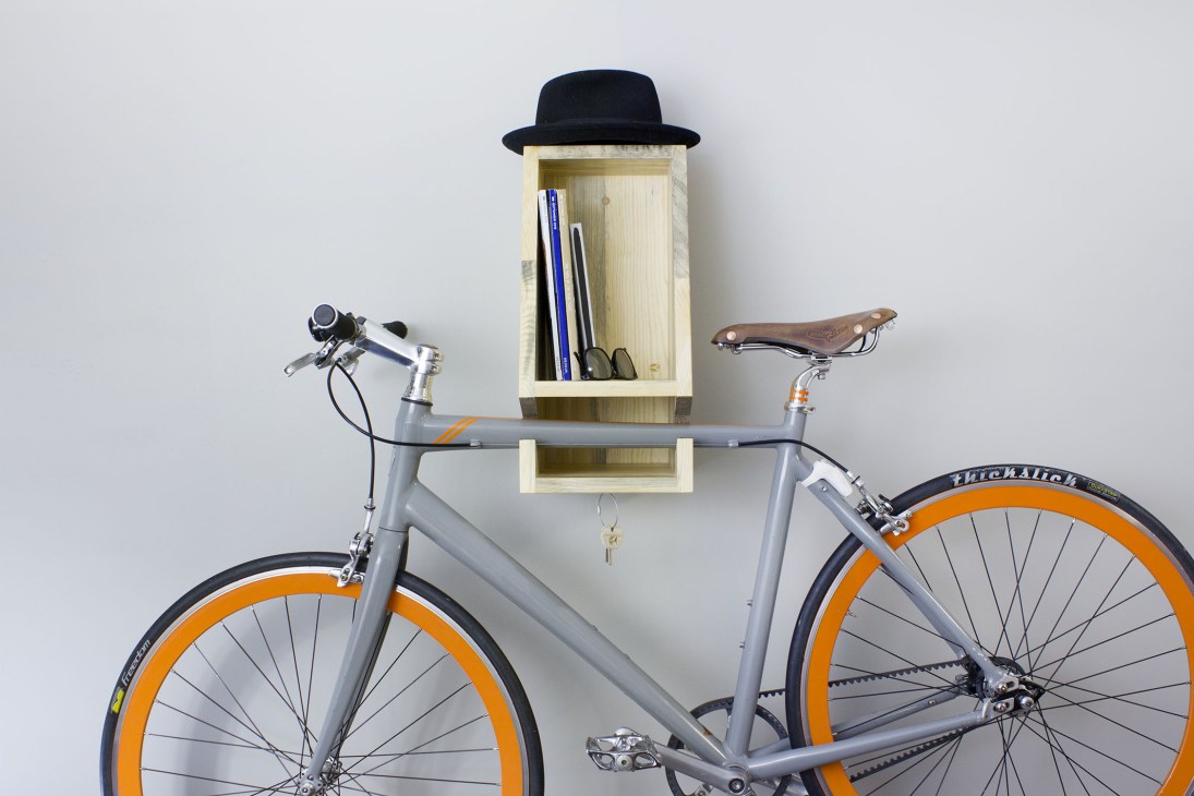 Gray fixed-gear bicycle with orange wheels mounted on a wooden wall-mounted bike rack with a black fedora hat above it.