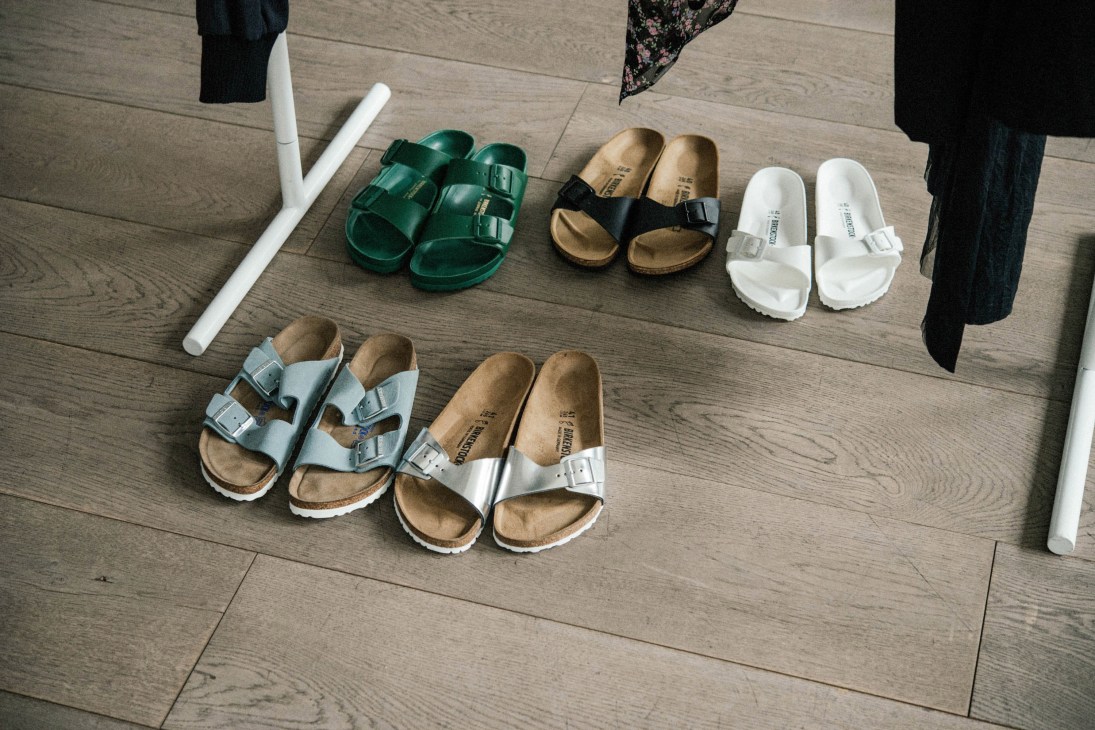 Collection of Birkenstock sandals in various colors displayed on wooden floor.