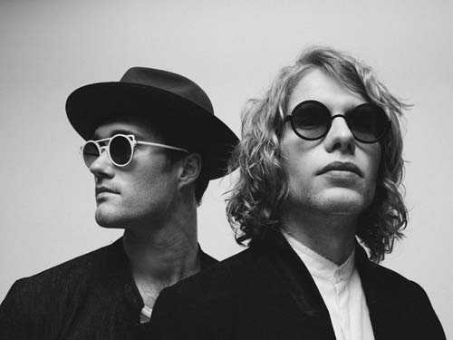 Two men wearing sunglasses and dark clothing pose together in a black and white photograph.
