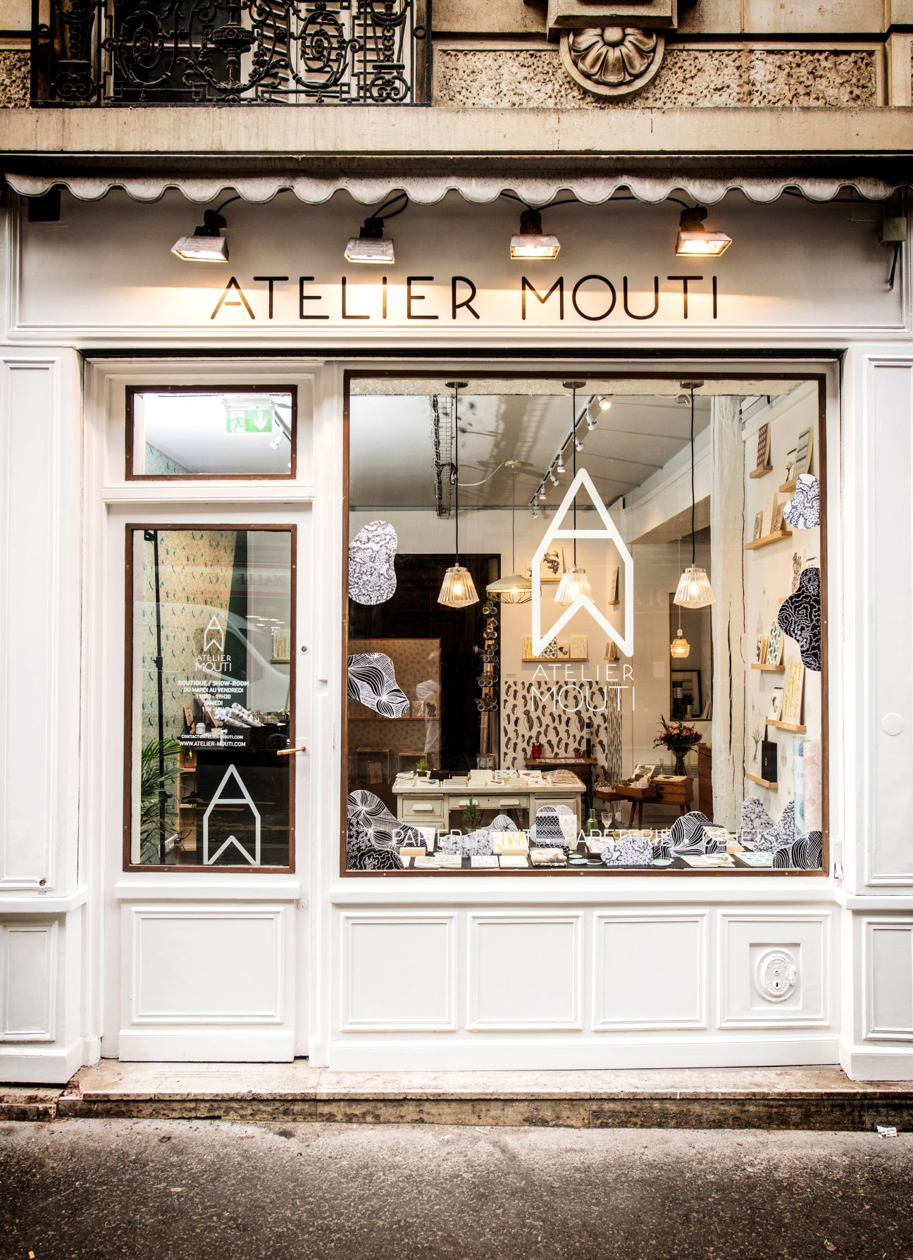 Atelier Mouti storefront in Paris with white facade, large windows displaying stationery and wallpaper designs.