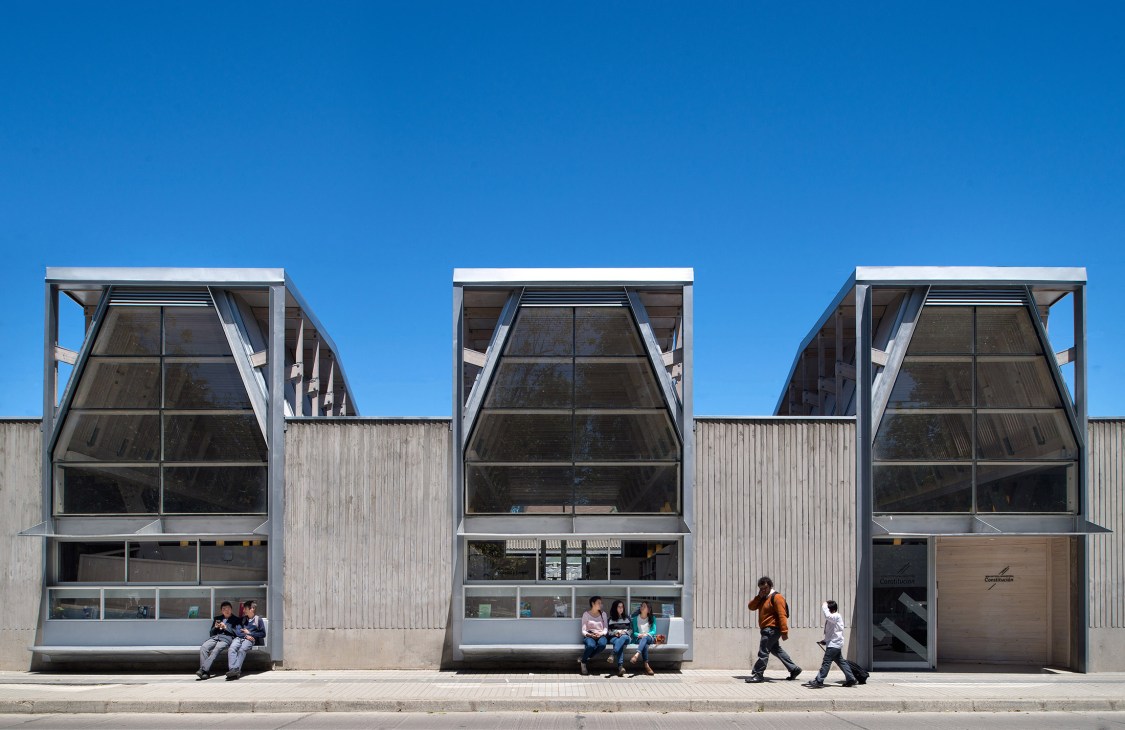 Modern waterfront building with large windows and metal framework in Constitución, Chile, with people sitting and walking outside.