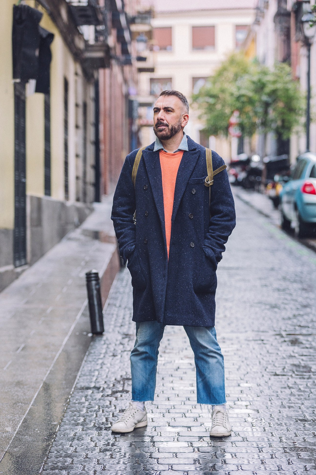 Man in navy coat and orange shirt standing on wet Madrid street