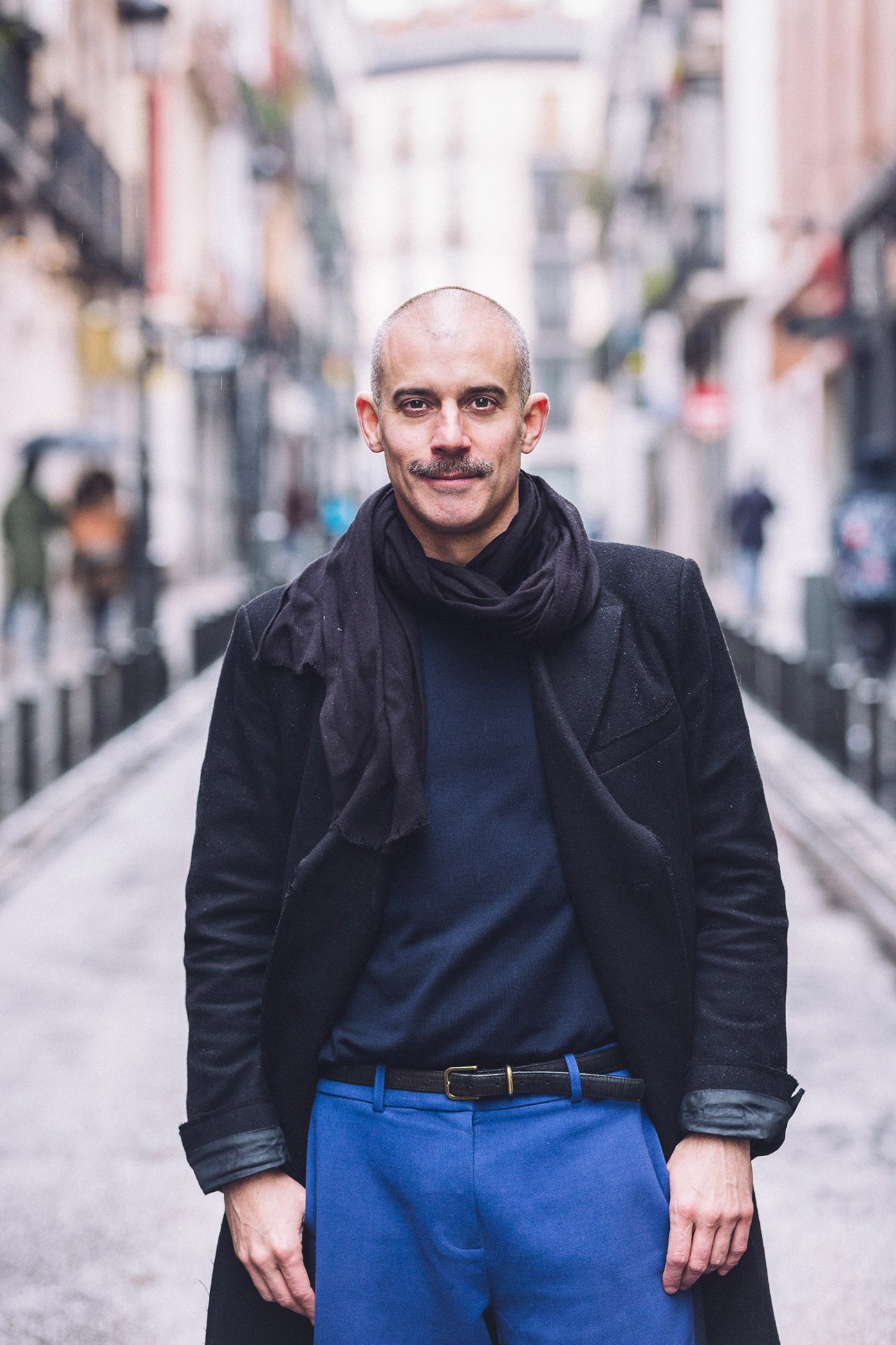 Man with mustache in black jacket and blue trousers standing on Madrid street