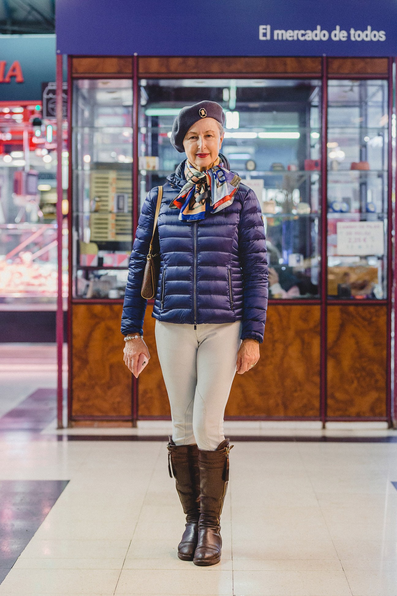 Woman in dark blue puffer jacket and white pants stands outside a storefront in Madrid.
