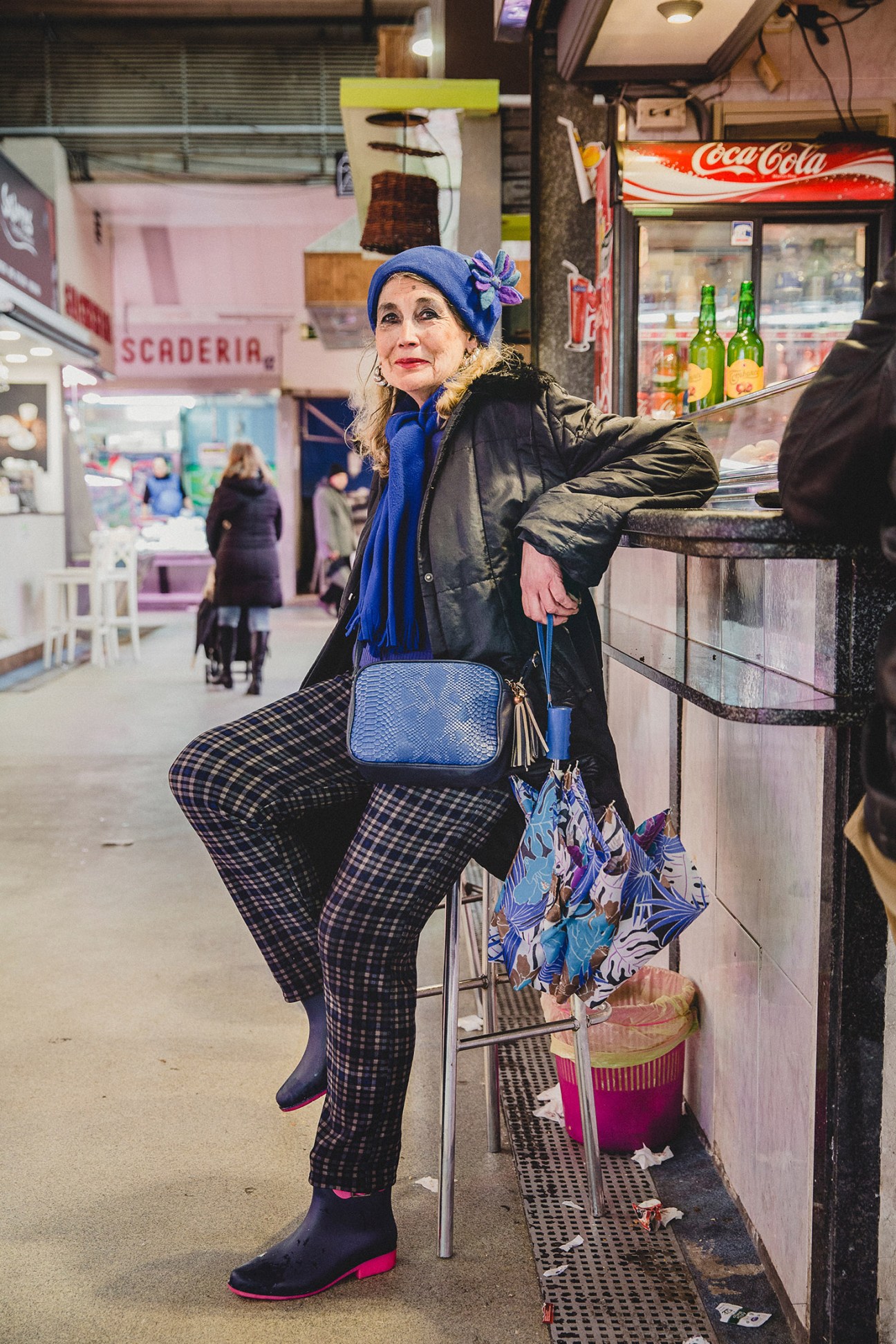 Woman in blue hat and checkered trousers standing in Madrid shopping arcade near Coca-Cola sign.