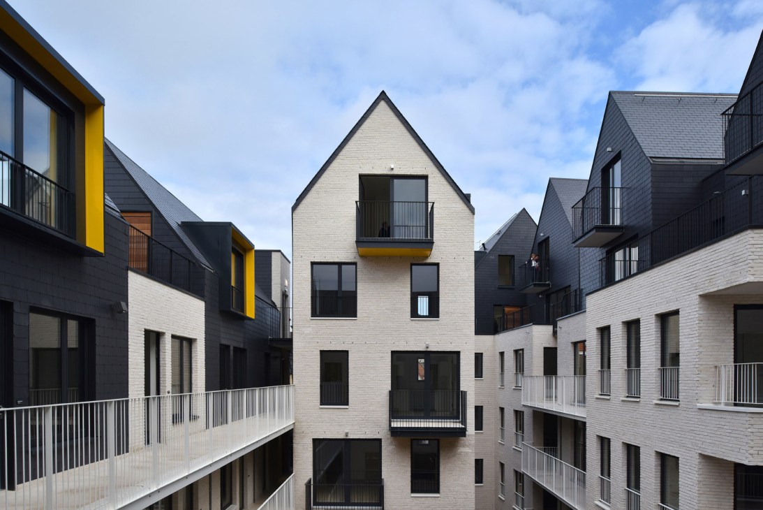 Modern residential buildings with white brick facades, pitched roofs, and yellow accents arranged around a pedestrian courtyard.