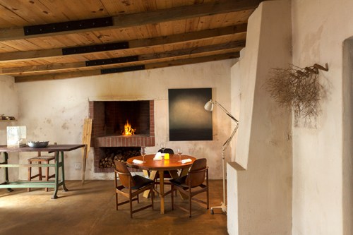 Interior of Wolfgat restaurant with wooden beams, fireplace, dining table and chairs in a whitewashed cottage.