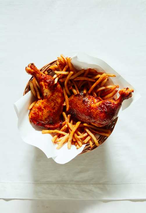 Two roasted chicken legs with crispy golden French fries served in white paper.