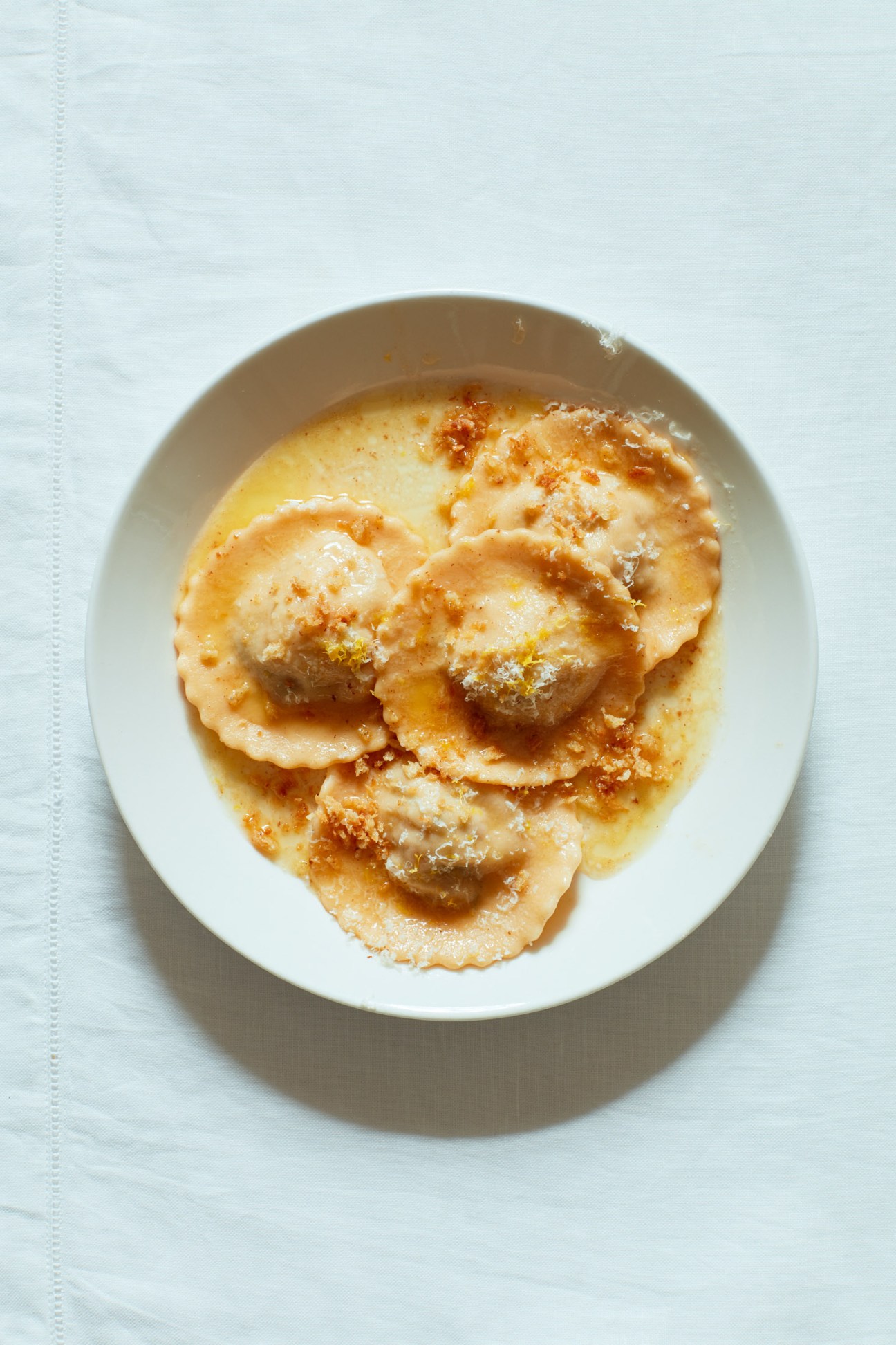 Crab ravioli with lemon butter sauce and crispy panko breadcrumb topping on a white plate.