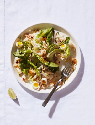 Crab and quail egg salad with avocado, fennel, lettuce, and crispy chilli oil on a white plate.