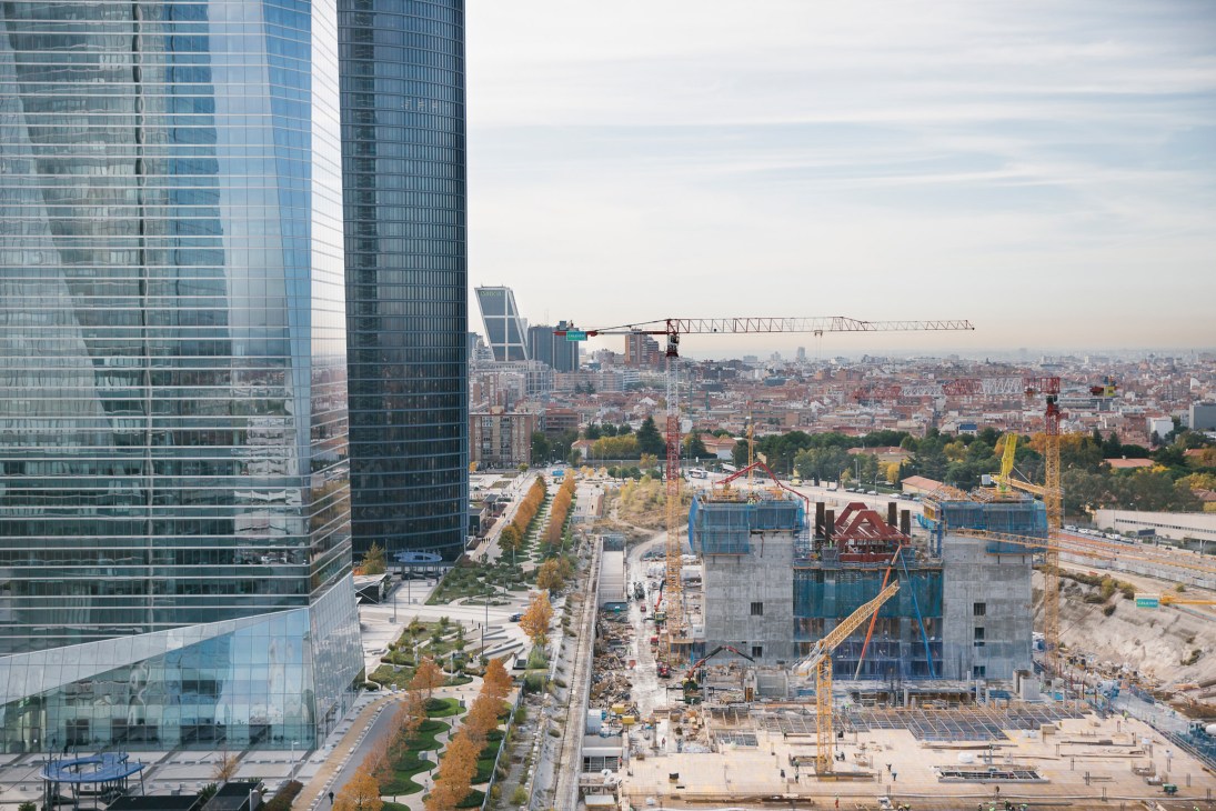 Madrid skyline with glass skyscrapers, construction cranes, and concrete building foundations under development.