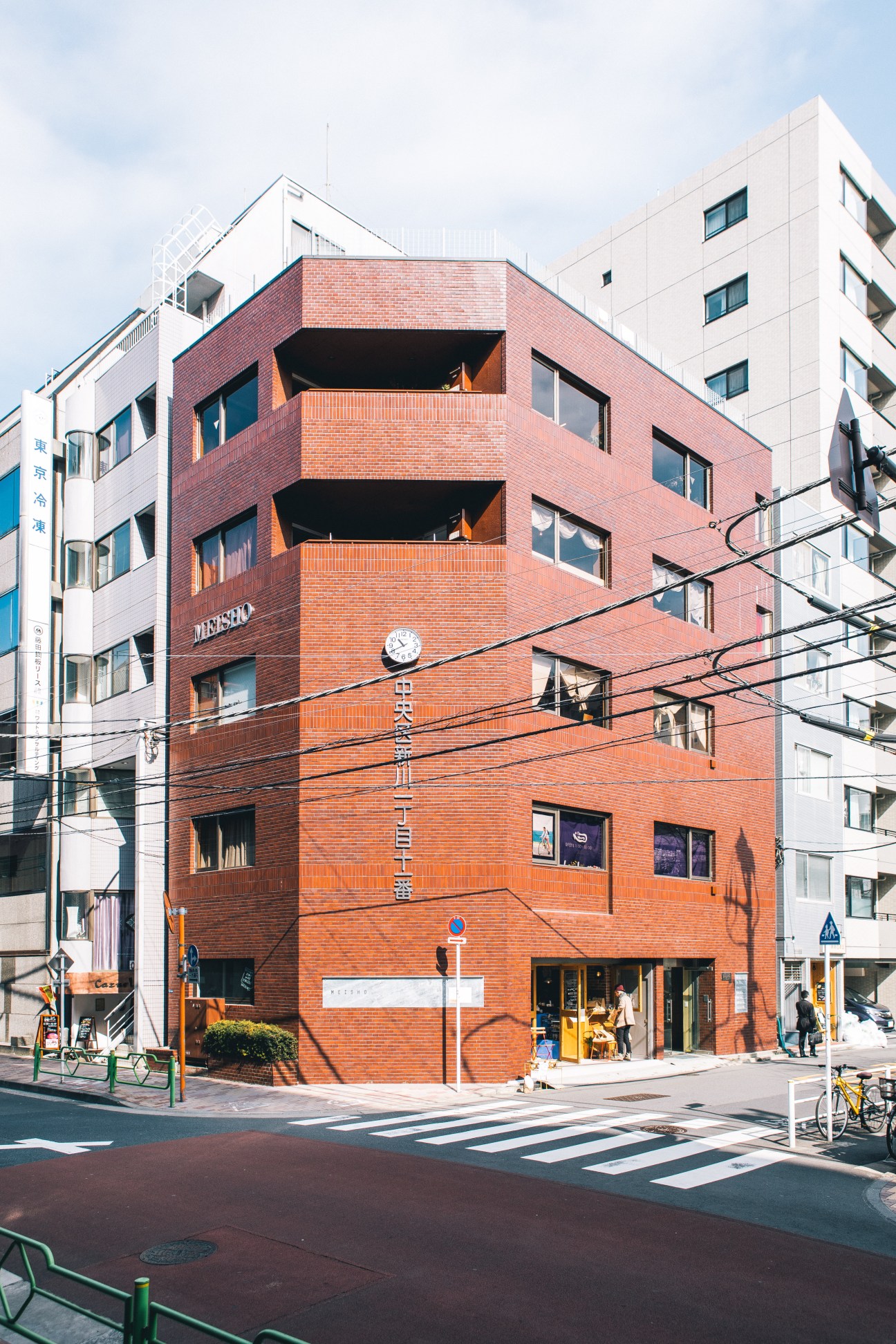Red brick Meisho Building in Tokyo with ground-floor café, gallery space, and mixed-use residential and commercial spaces.