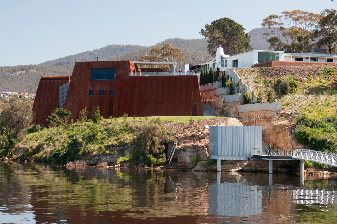 Museum of Old and New Art in Hobart with distinctive rust-colored angular architecture overlooking the Derwent River and forested hills.