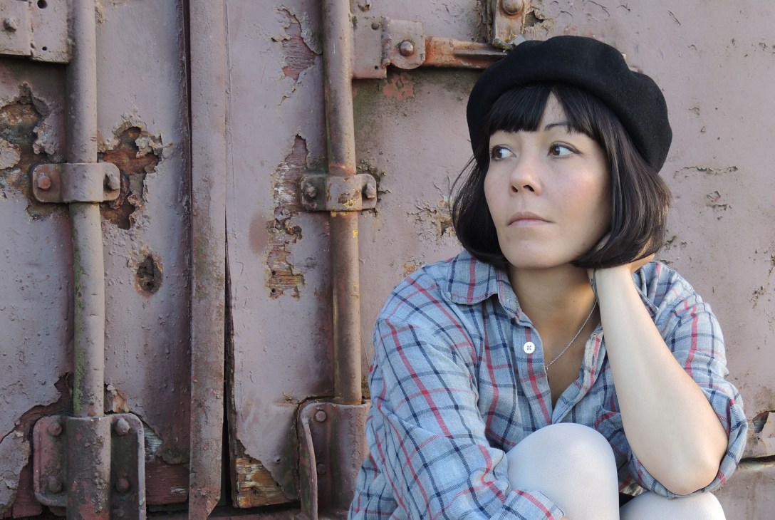 Woman in plaid shirt and black beret posing against weathered industrial metal door.