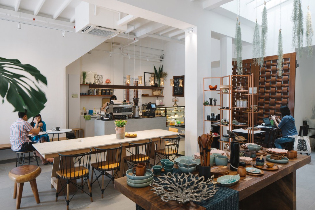 Interior of Groundstory café and gallery in Singapore showing wooden shelving, ceramics, plants, and customers seated at tables.