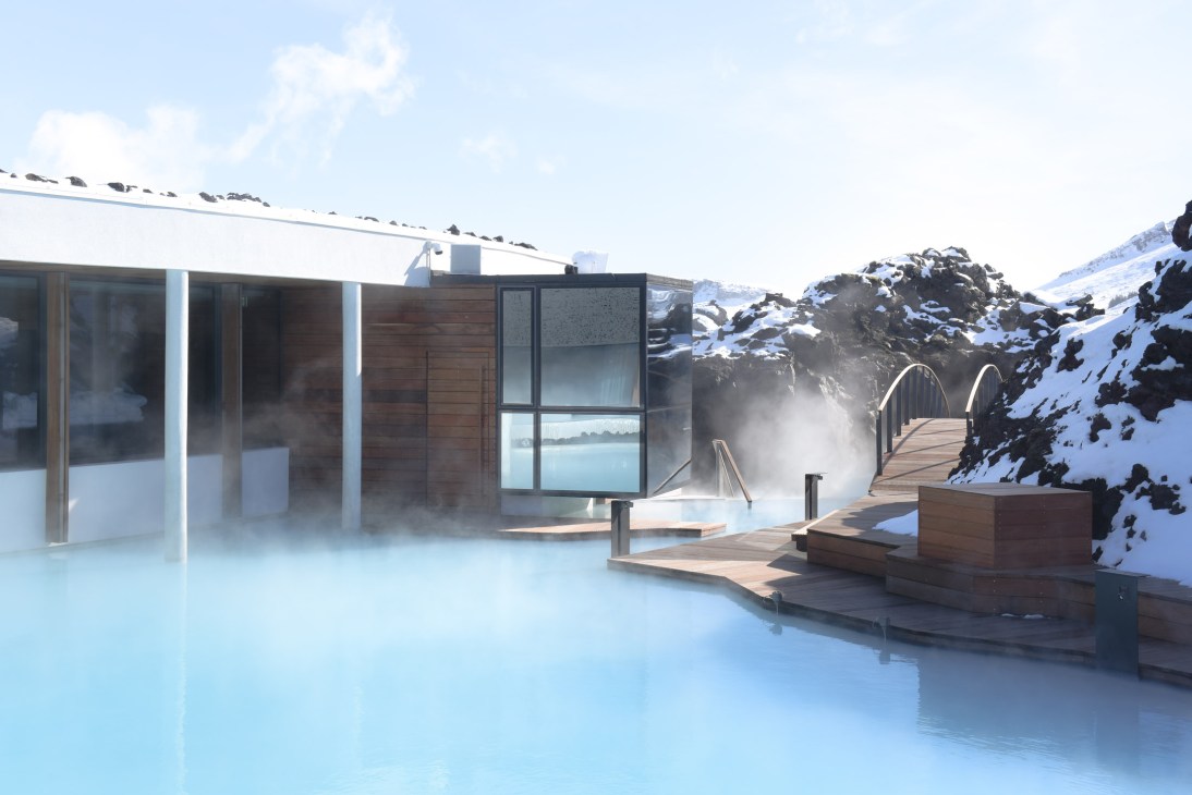 The Retreat Hotel at Blue Lagoon with minimalist grey building overlooking geothermal turquoise water and snow-covered lava rock landscape in Iceland.