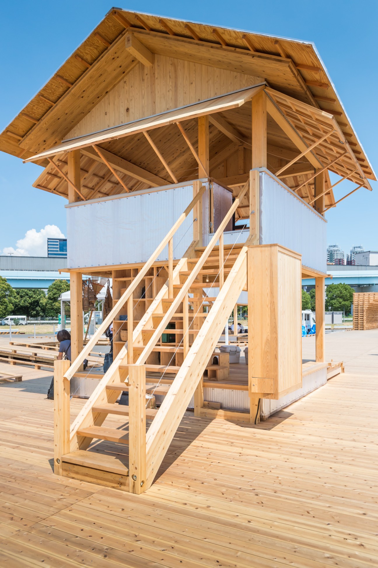 Wooden tower structure with stepped exterior stairs and open framework design against clear blue sky.