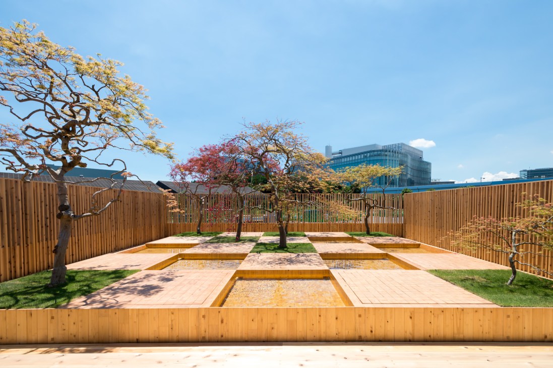 Checkerboard Water Garden with maple trees in various colors framed by wooden fencing and modern buildings beyond.