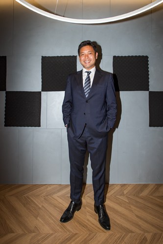 Man in navy suit standing in modern interior space with geometric wall panels.
