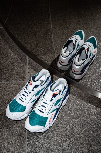 Two pairs of Mizuno trainers with teal and white colorways displayed on grey pavement.