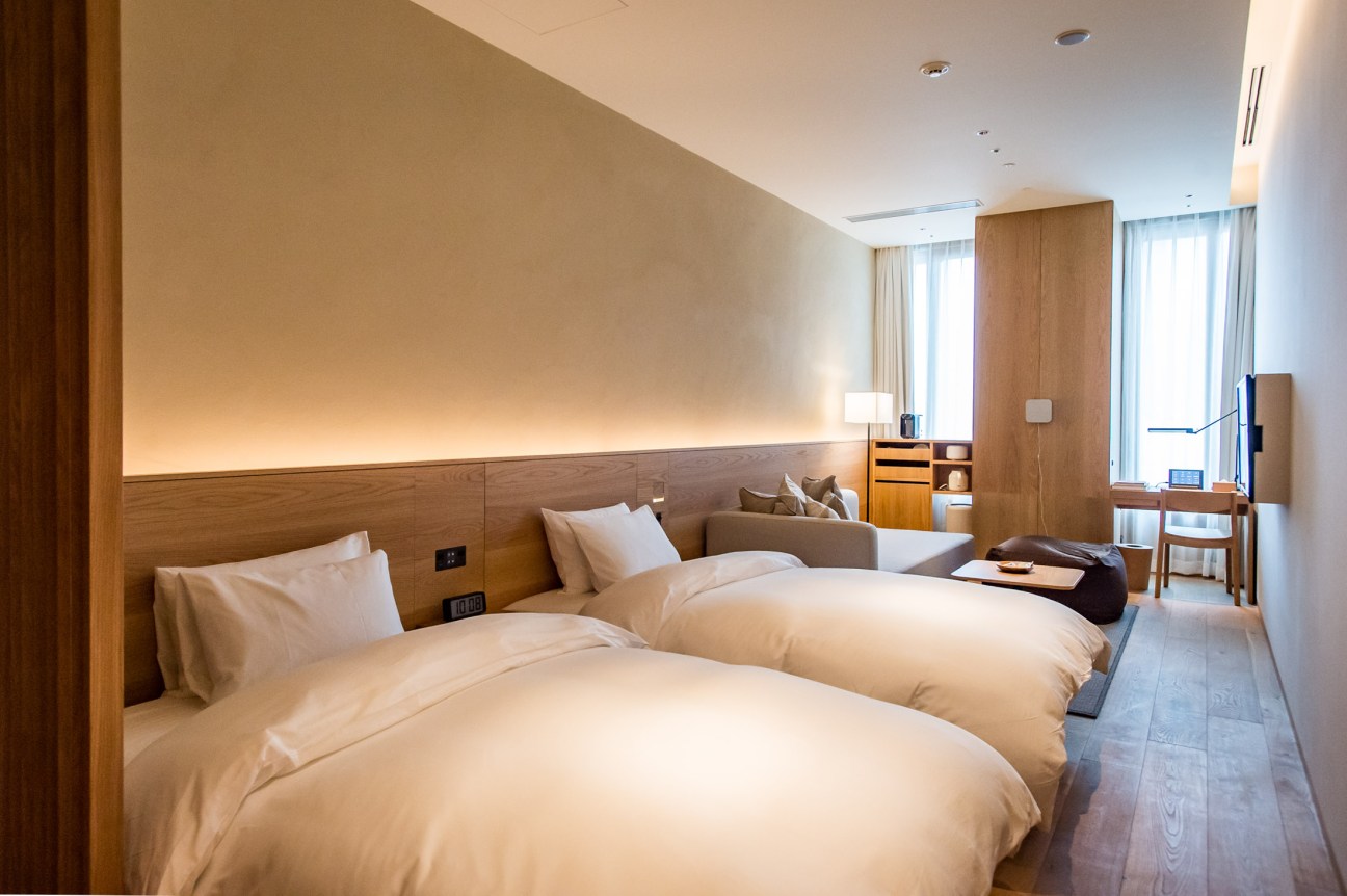 Minimalist hotel room with two beds, wooden furnishings, and neutral tones at Muji Hotel Tokyo.