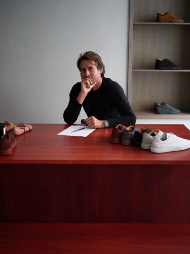 Adam Lewenhaupt, founder of CQP leather shoe brand, sits at a red table with shoe samples displayed.