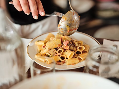 Hand holding a spoon of pasta with peppers and rigatino over a plate of pasta at Reinhard Plank in Florence.