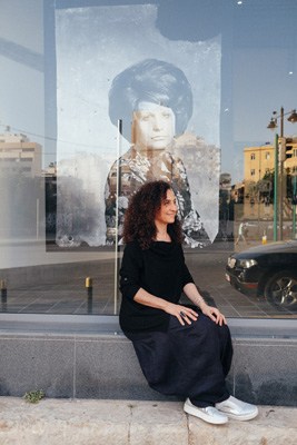 Woman sitting in front of a large portrait artwork displayed on a building facade in Beirut.