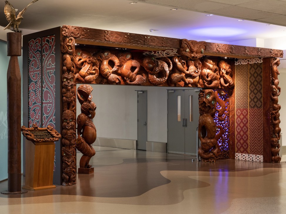Ornately carved wooden archway with intricate decorative details in an airport terminal interior.