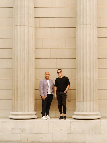 Thomas Hugo Møller and another man stand between two large white classical columns against a beige building facade.