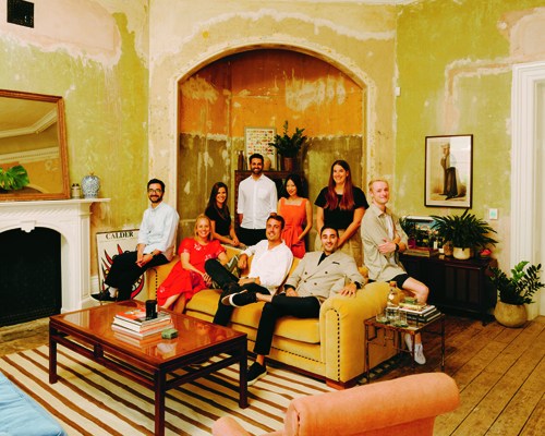 Group portrait of Ennismore team members posed together in a bright, yellow-walled interior space with arched doorway.