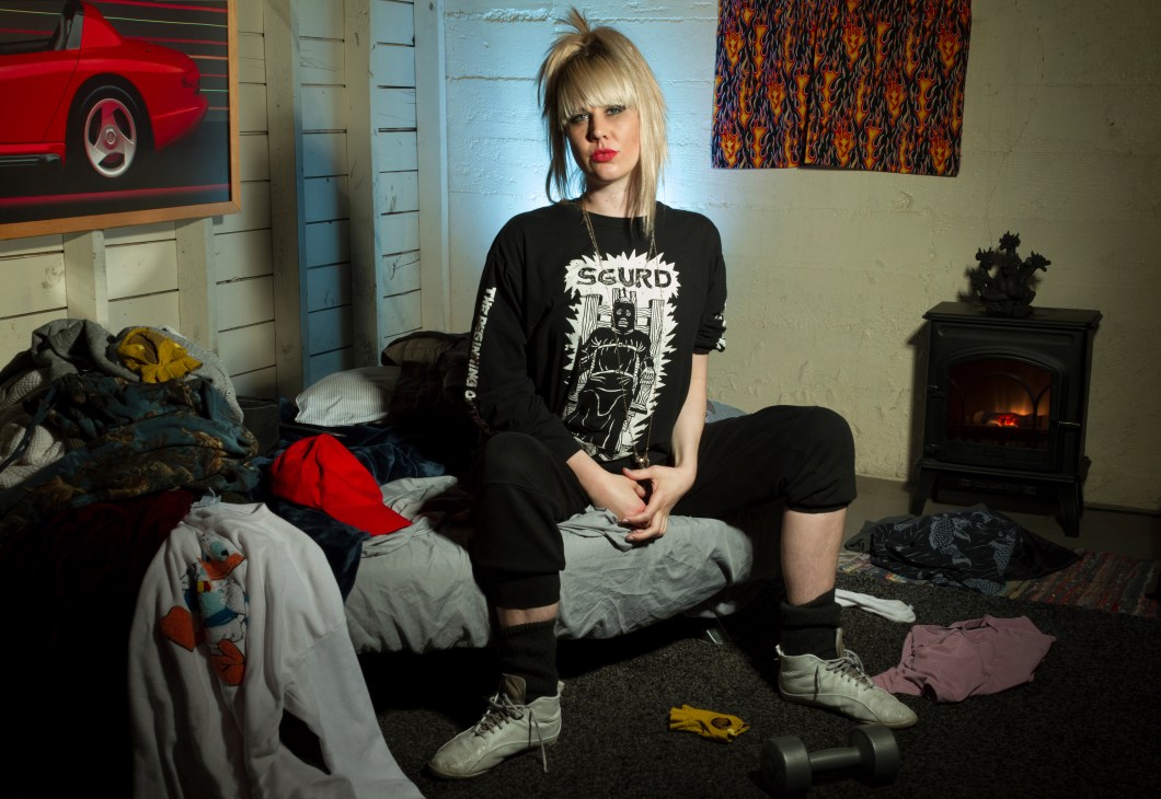 Person sitting on bed in messy bedroom with guitar and fireplace visible