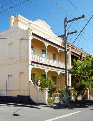 Victorian-era terrace house with cream-colored facade, ornate balconies, and ivy-covered walls in Melbourne.