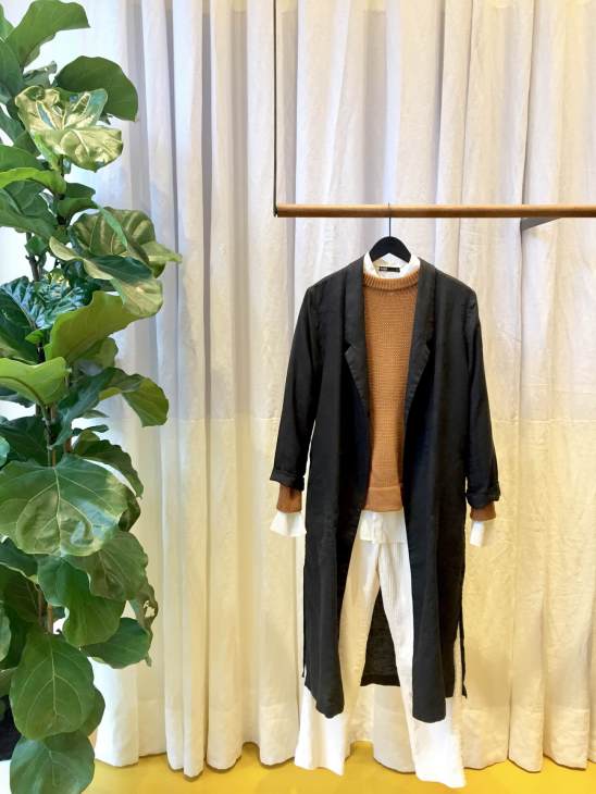 Handred clothing displayed on hanger: black cardigan over mustard sweater and white pleated skirt.