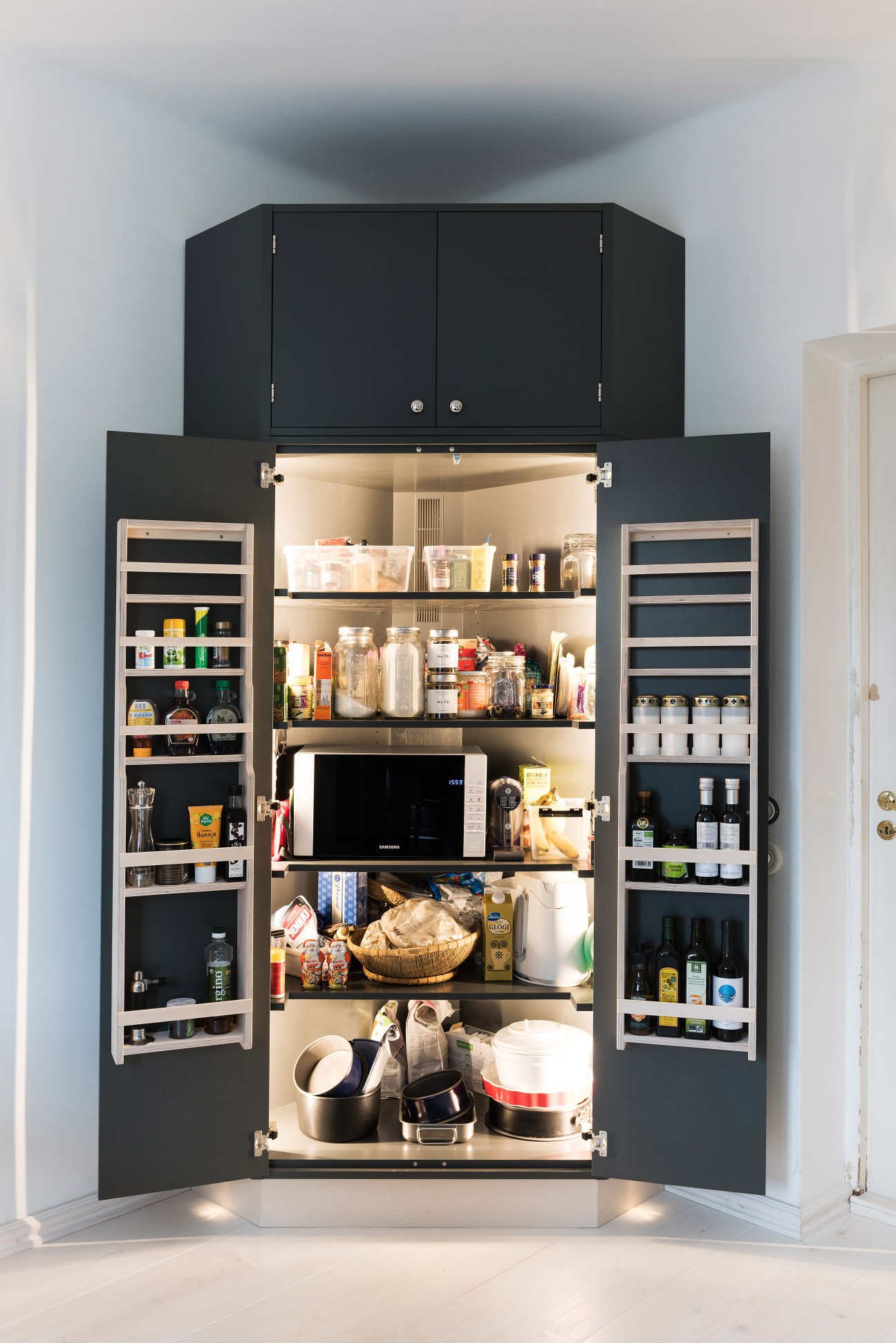 Open black kitchen cabinetry unit with organized shelves displaying kitchenware, jars, and appliances.