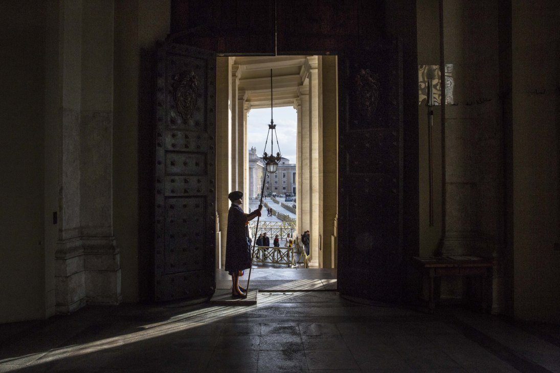 Swiss guard standing in a Vatican loggia doorway overlooking St Peter's Square.