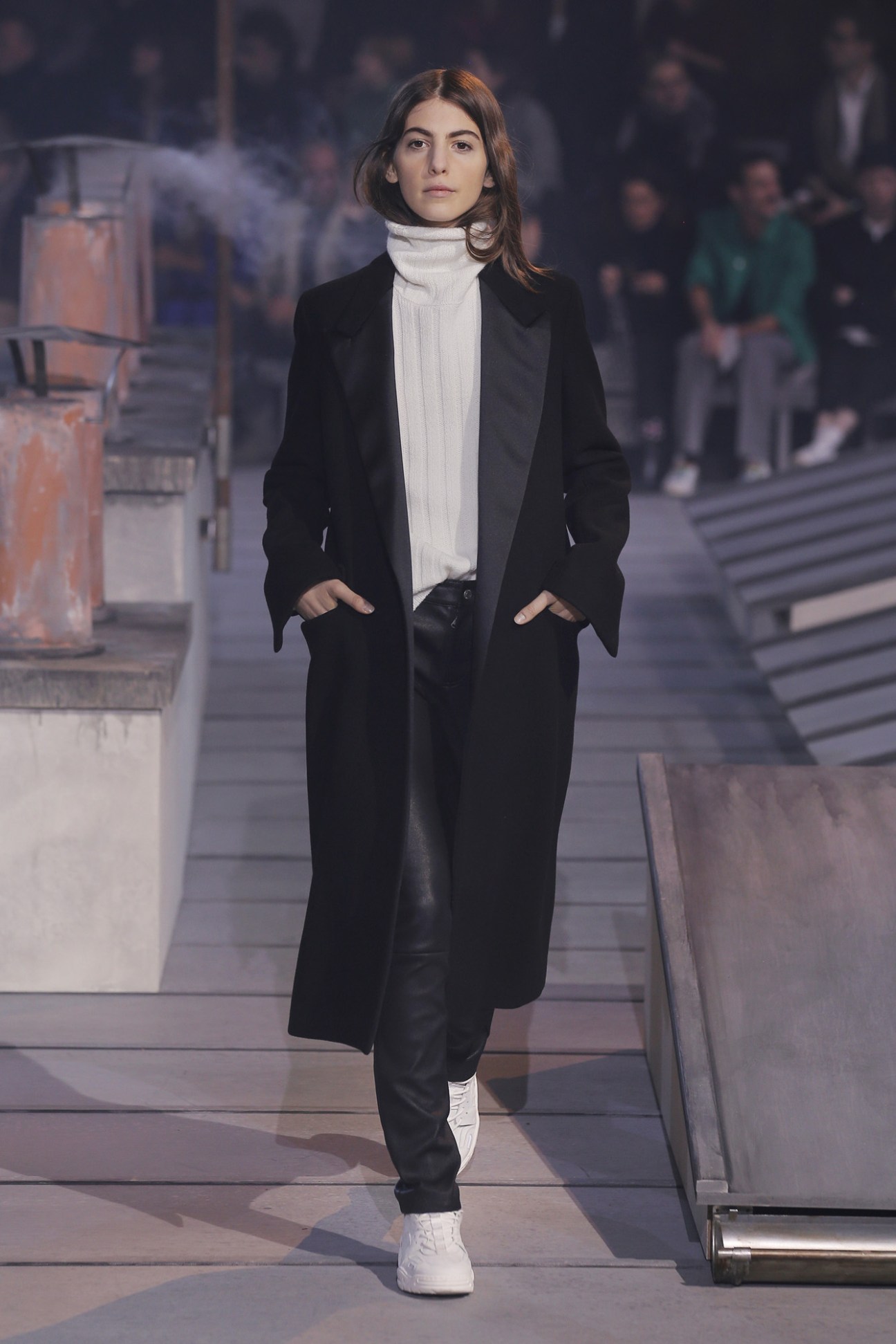 Model wearing Ami men's sweater, women's double-breasted coat, leather trousers and trainers on runway.