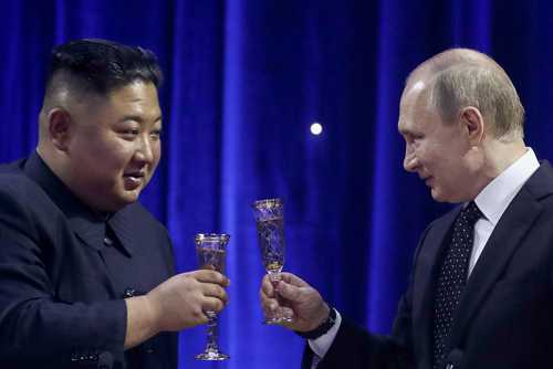 Vladimir Putin and Kim Jong-un toast with glasses against a blue curtain backdrop.
