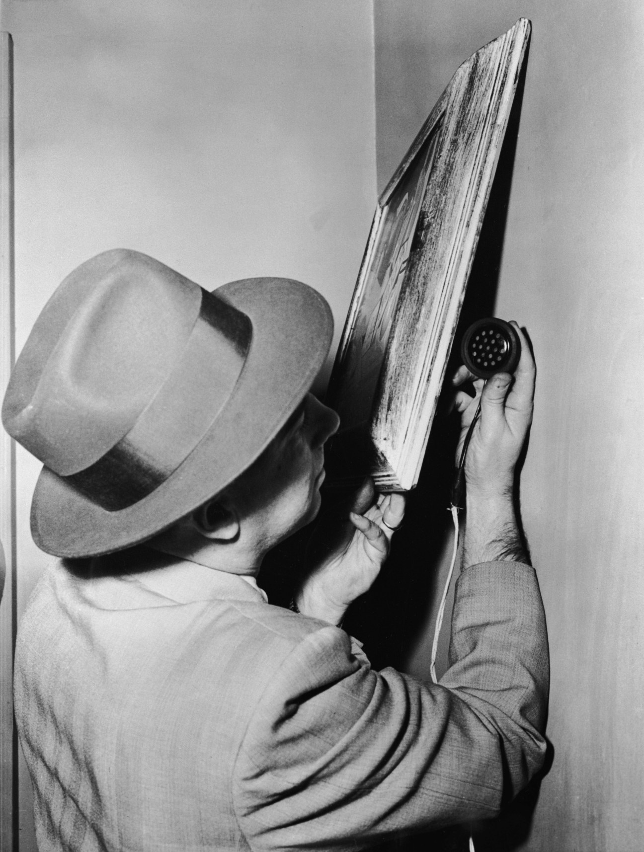 Black and white photograph of a man in a hat using a spray application tool on a large wooden board.