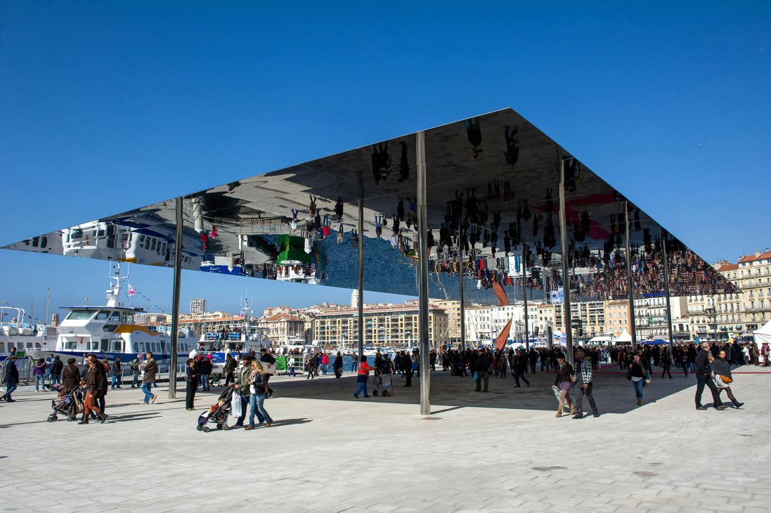 Marseille waterfront with modern architecture and crowd of visitors under a mirrored canopy structure.
