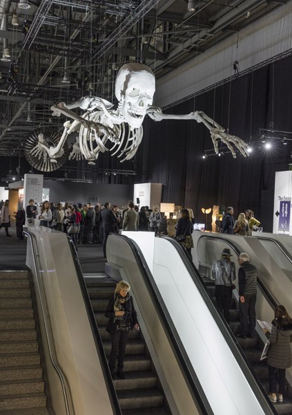 Large skeletal sculpture suspended above escalators in a modern museum atrium during opening day.