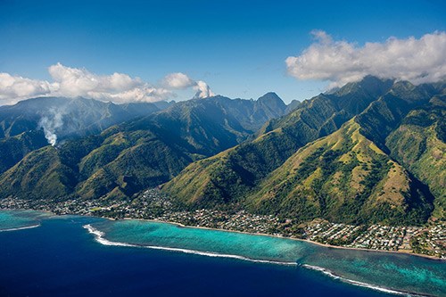 Aerial view of lush green mountains meeting turquoise ocean waters in French Polynesia.