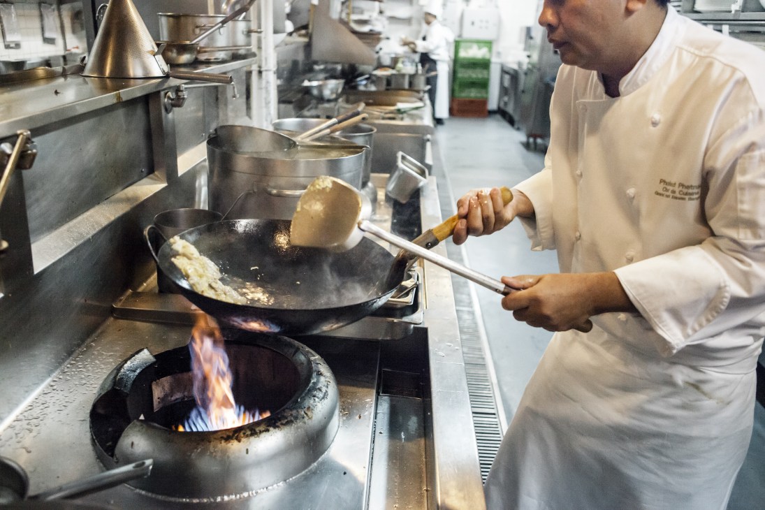 Chef stir-frying khao phad kai dao in a wok over open flame in hotel kitchen.