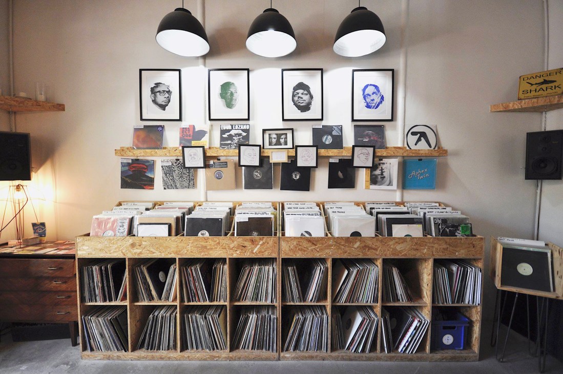Interior of Extend & Play record shop in Marseille with wooden storage bins filled with vinyl records, framed artwork on walls, and pendant lighting.