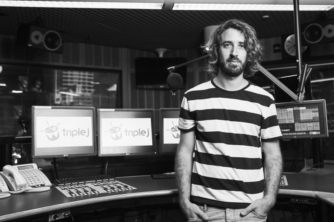 Nick Findlay, music director at Triple J, standing in a radio studio wearing a striped shirt.