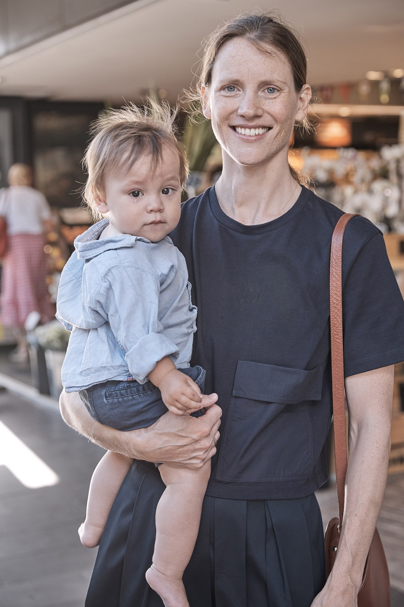 A woman holds a young child in her arms while standing in an indoor shopping area.