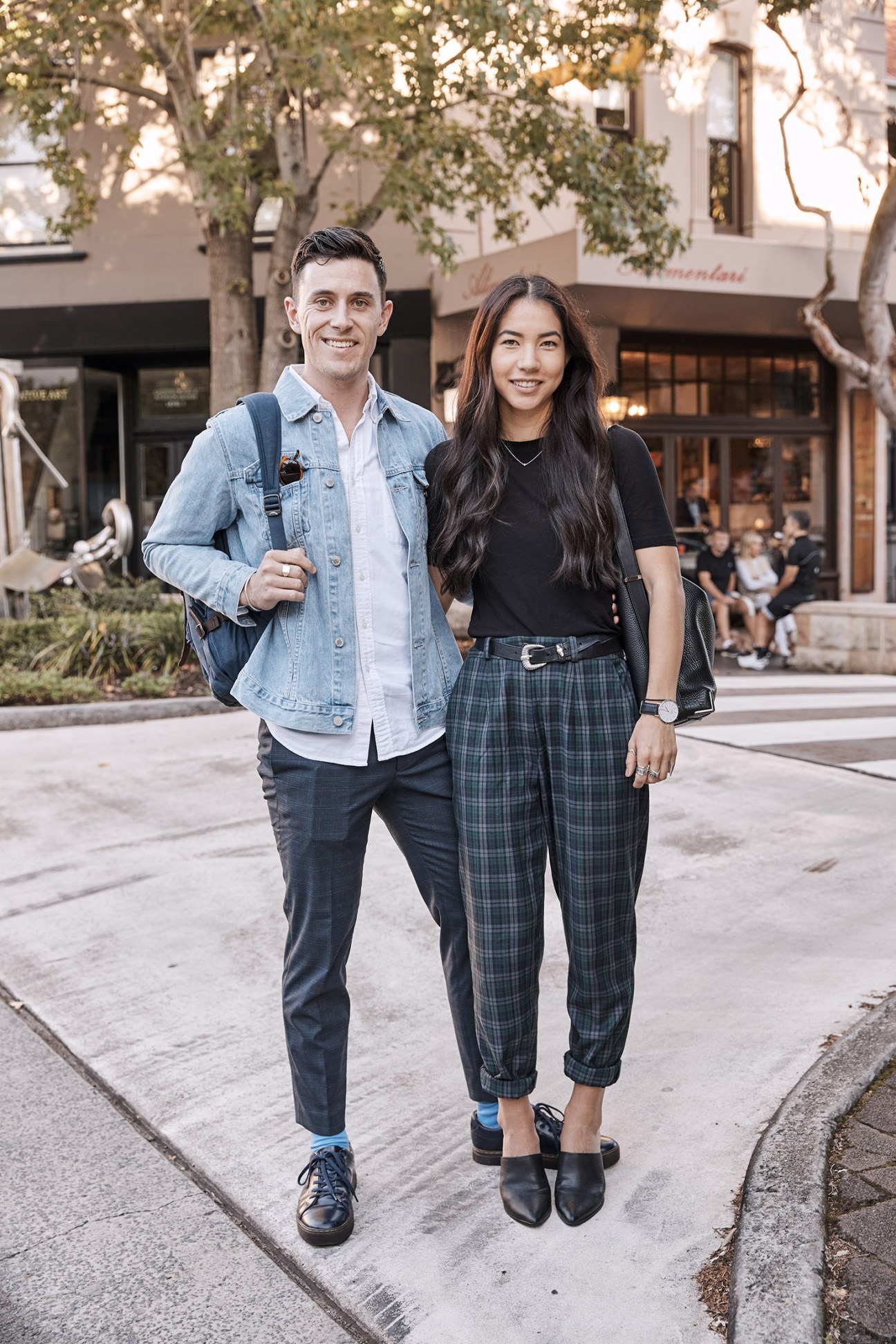 Two young professionals smile while standing on a city street with storefronts in the background.